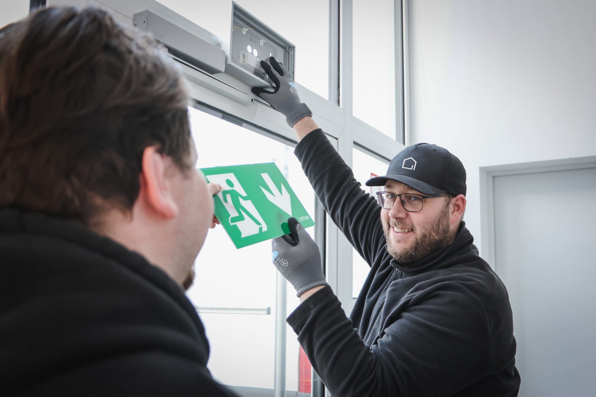 OPASA Techniker setzen ein Rettungszeichen in eine Sicherheitsleuchte über einer Glastür ein