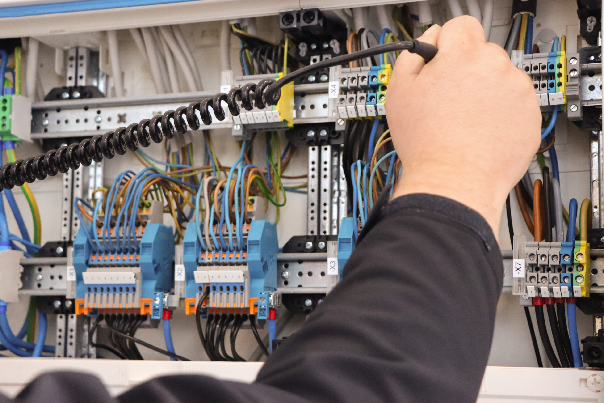 Elektriker prüft eine elektrische Schalttafel mit Messgerät und kontrolliert die Verkabelung.